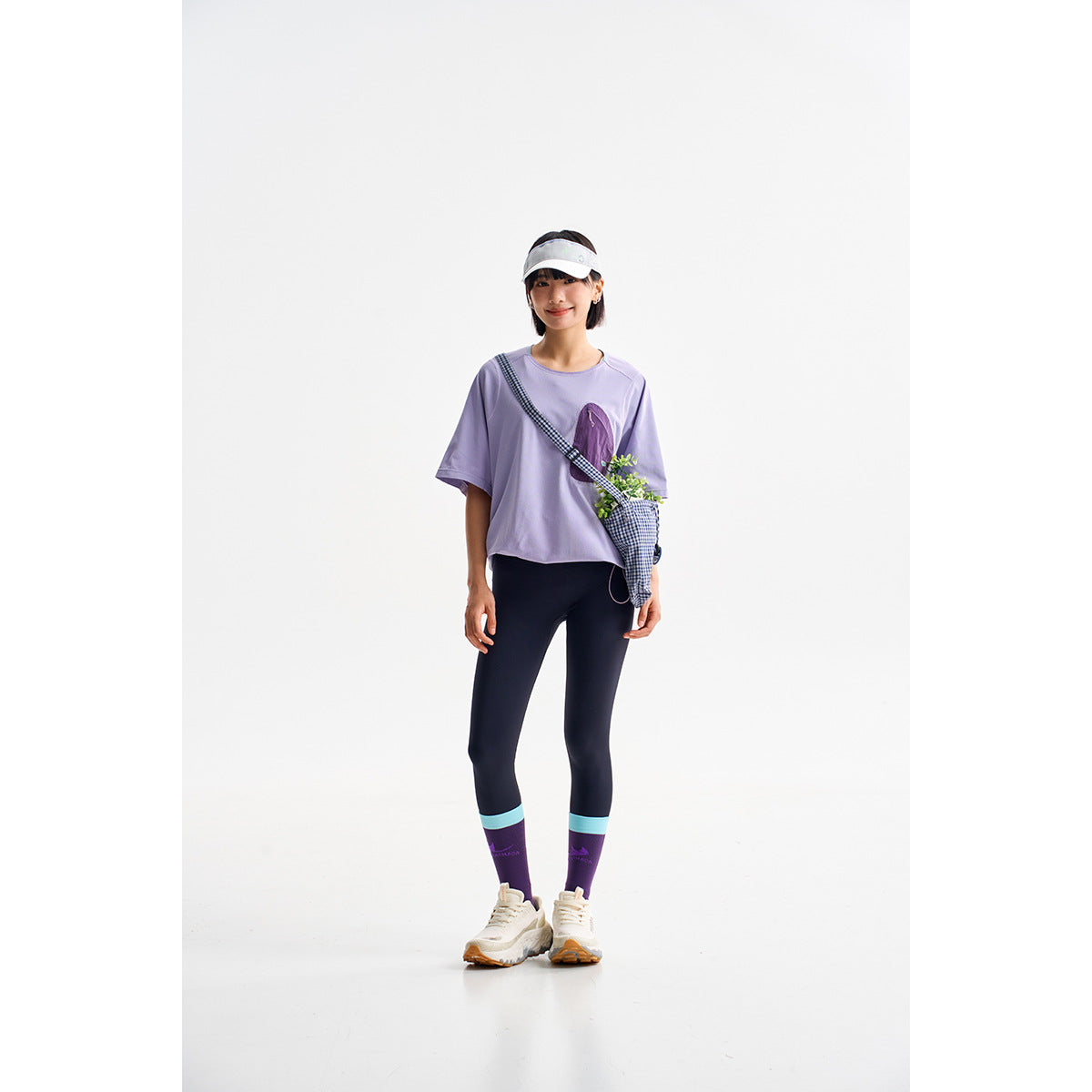 Model wearing a lavender short-sleeve top with a purple chest pocket and navy leggings with turquoise and purple cuffs.
