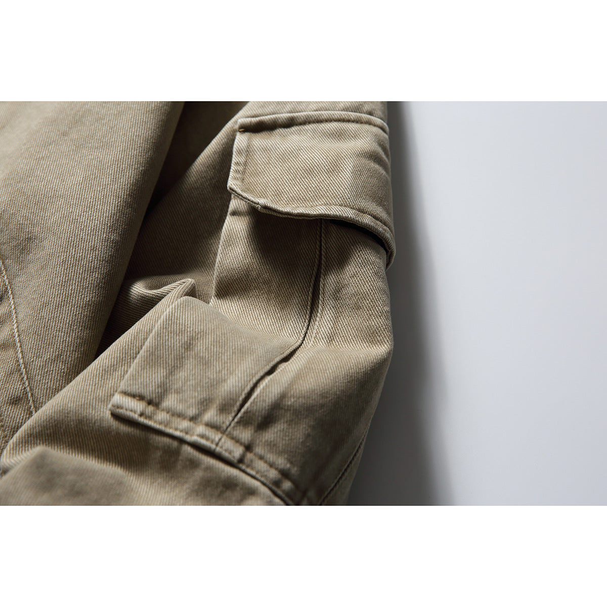 Close-up of the taupe jacket's sleeve flap pocket, stitching, and fabric texture.