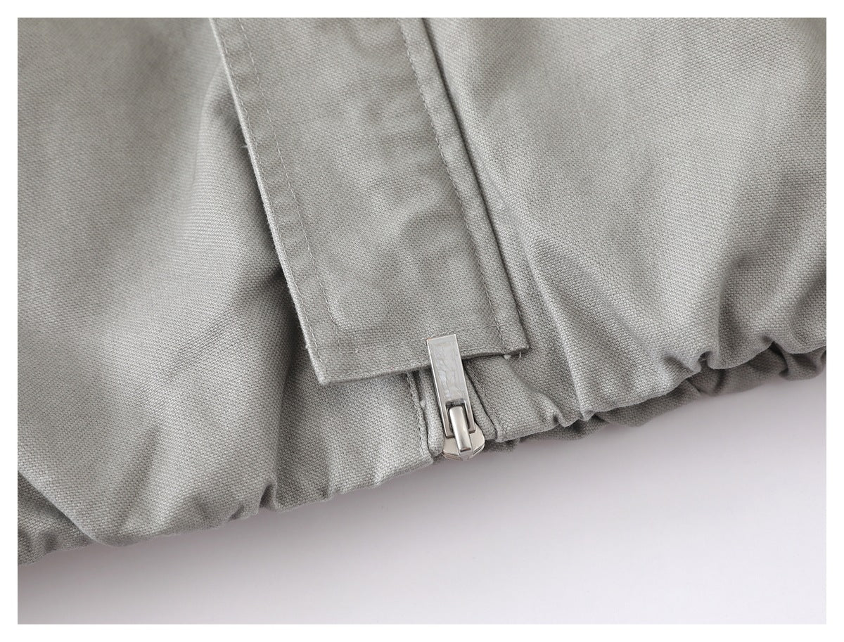 Close-up of a silver zipper and gathered hem on the light gray jacket.