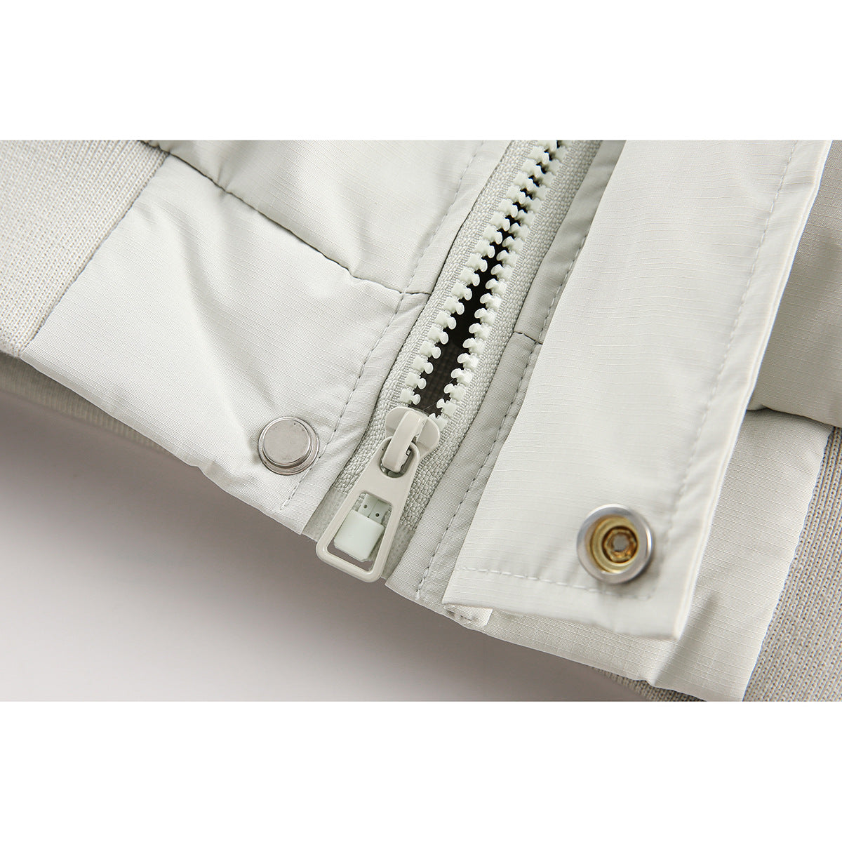 Close-up of a pale jacket's chunky zipper, snap fasteners, and stitched panels.