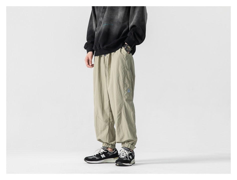 Cropped model wearing loose light khaki jogger pants with elastic cuffs and a small blue leg emblem.