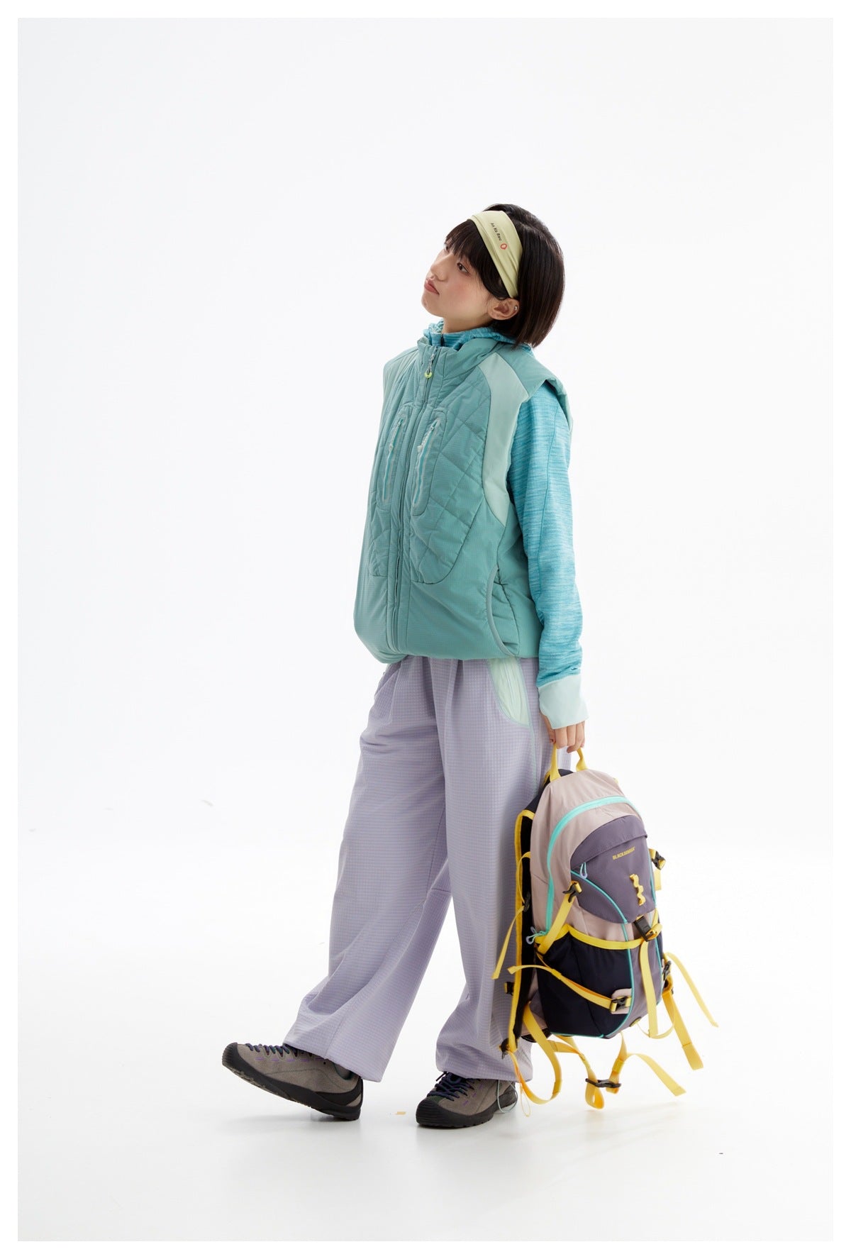 Side view of a model wearing a teal quilted zip vest with a hood and zippered chest pockets.
