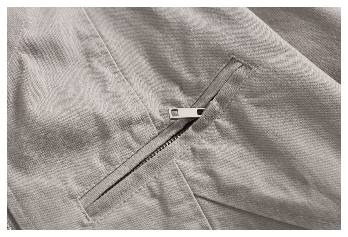 Close-up of a diagonal zipper pocket on a light gray jacket, showing its metal pull and stitched seams.