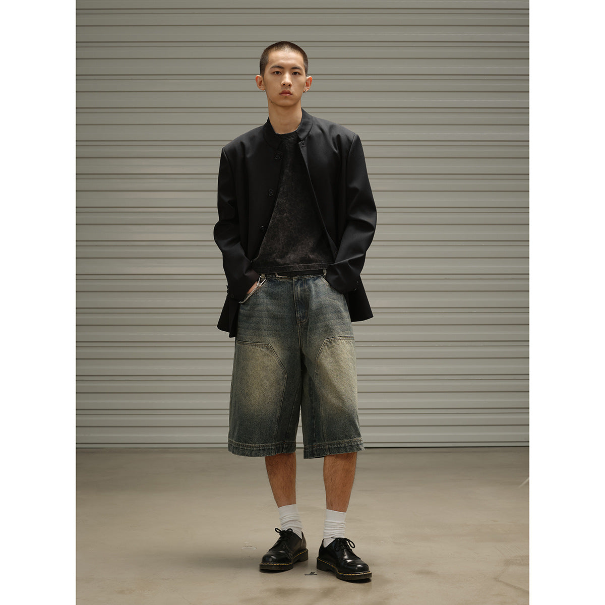 Full-length model wearing an open black band-collar coat over a dark top with oversized faded denim shorts.