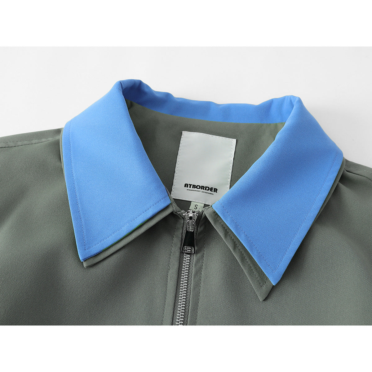 Close-up of a gray-green jacket with a bright blue pointed collar, front zipper, and visible sewn-in neck label.