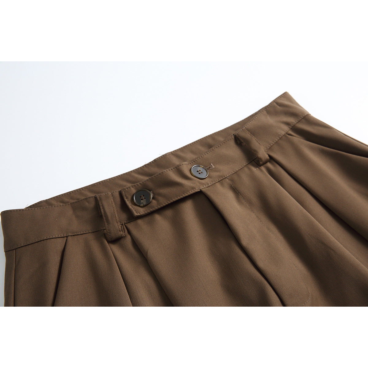 Close-up of brown shorts showing the waistband, two buttons, belt loops and front pleats.