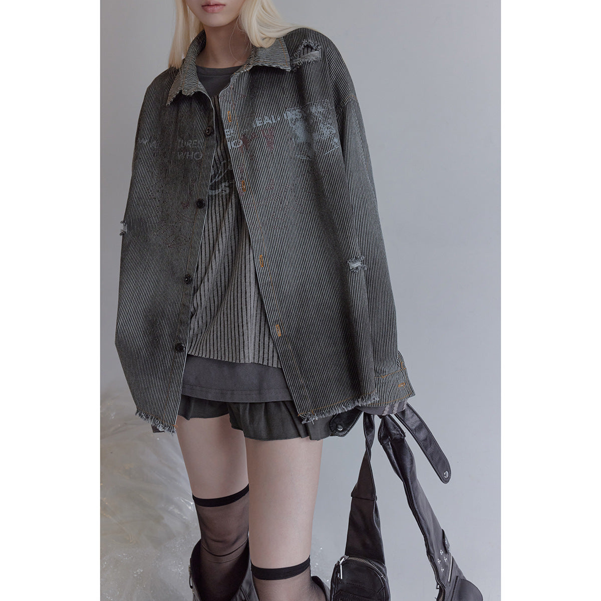 Cropped model wearing an oversized charcoal pinstriped jacket with distressed patches and frayed edges.