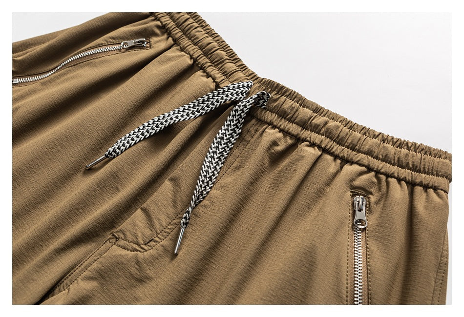 Close-up of tan shorts showing the elastic waistband, braided drawstring, and silver zip pockets.