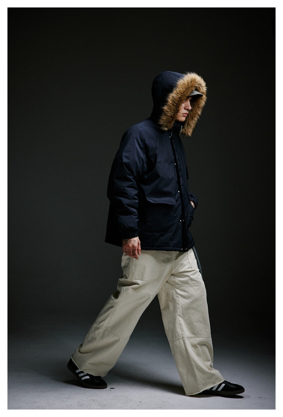 Side view of a model wearing a dark navy fur-trim hooded jacket while walking.