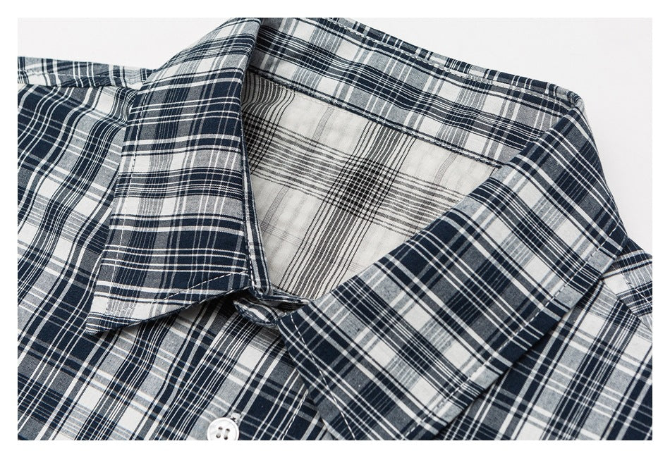 Close-up of the pointed collar and upper placket of a navy, gray, and white plaid button-up shirt.