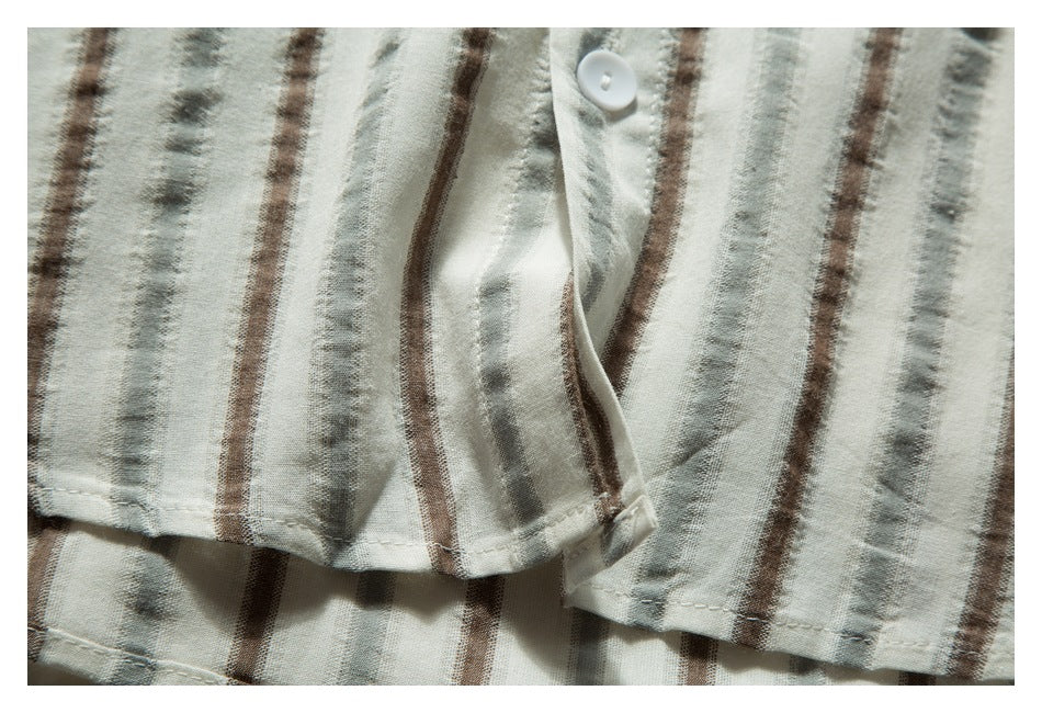 Close-up of an off-white garment with muted gray and brown stripes, a white button, and stitched edges.