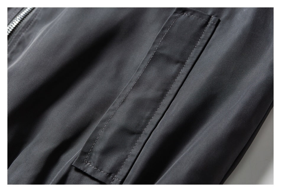 Close-up of a stitched pocket opening and zipper on dark charcoal fabric.
