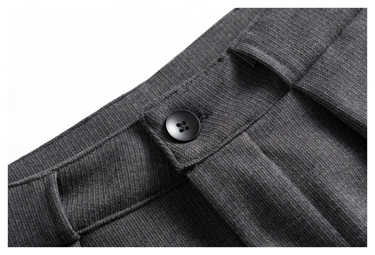 Close-up of charcoal gray trousers with a black waistband button and front pleat.