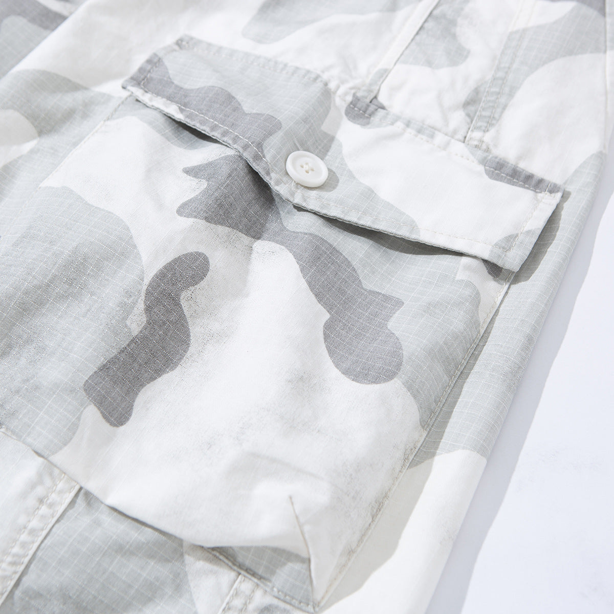 Close-up of gray and white camouflage shorts with a buttoned cargo pocket flap.