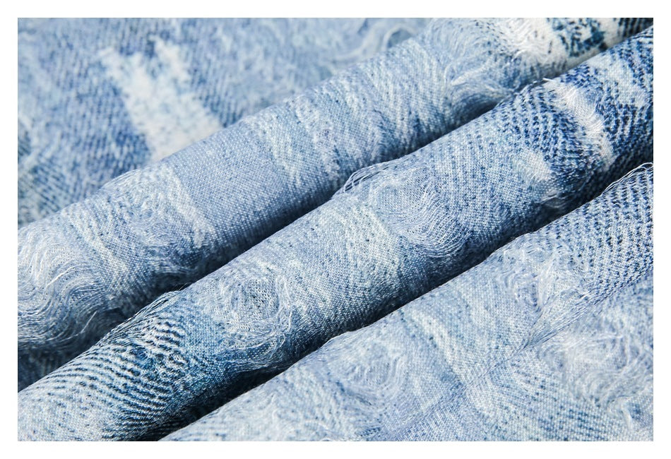 Close-up of pale blue patterned fabric draped in folds, with distressed patches and loose threads.
