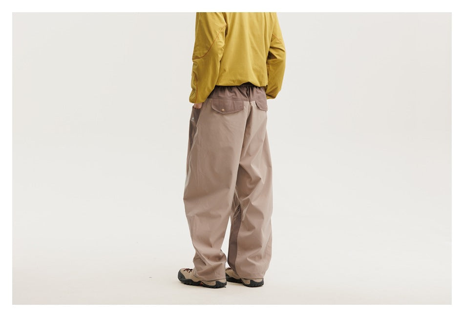 Rear view of a model wearing loose taupe trousers with an elastic waist and two flap back pockets.