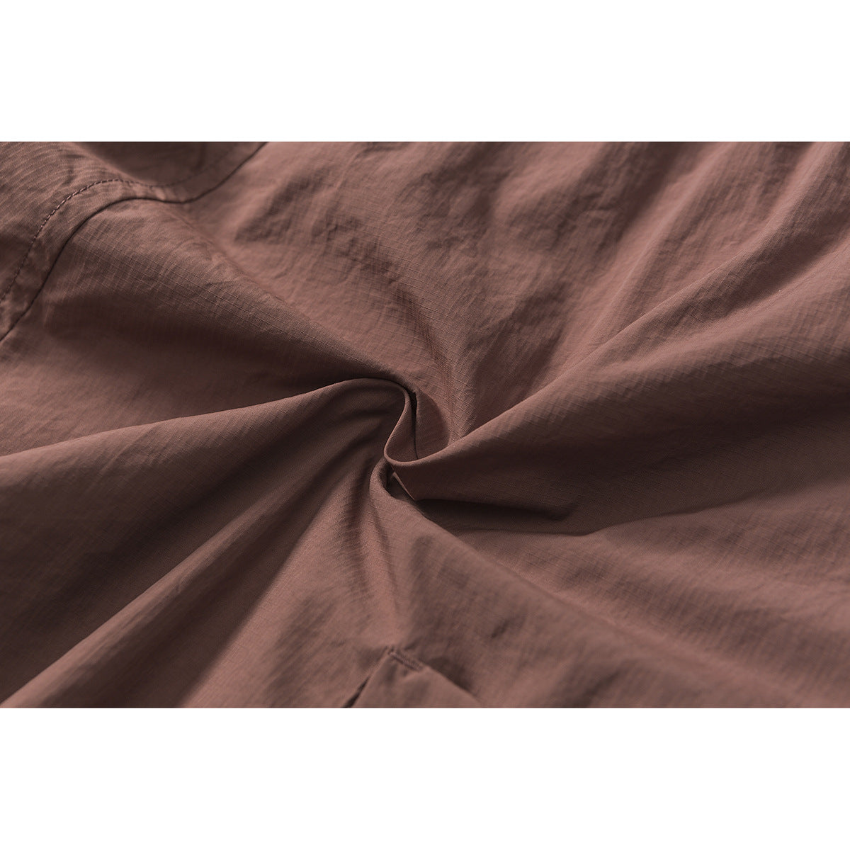 Close-up of dusty mauve shorts fabric gathered into folds, with a stitched seam visible.