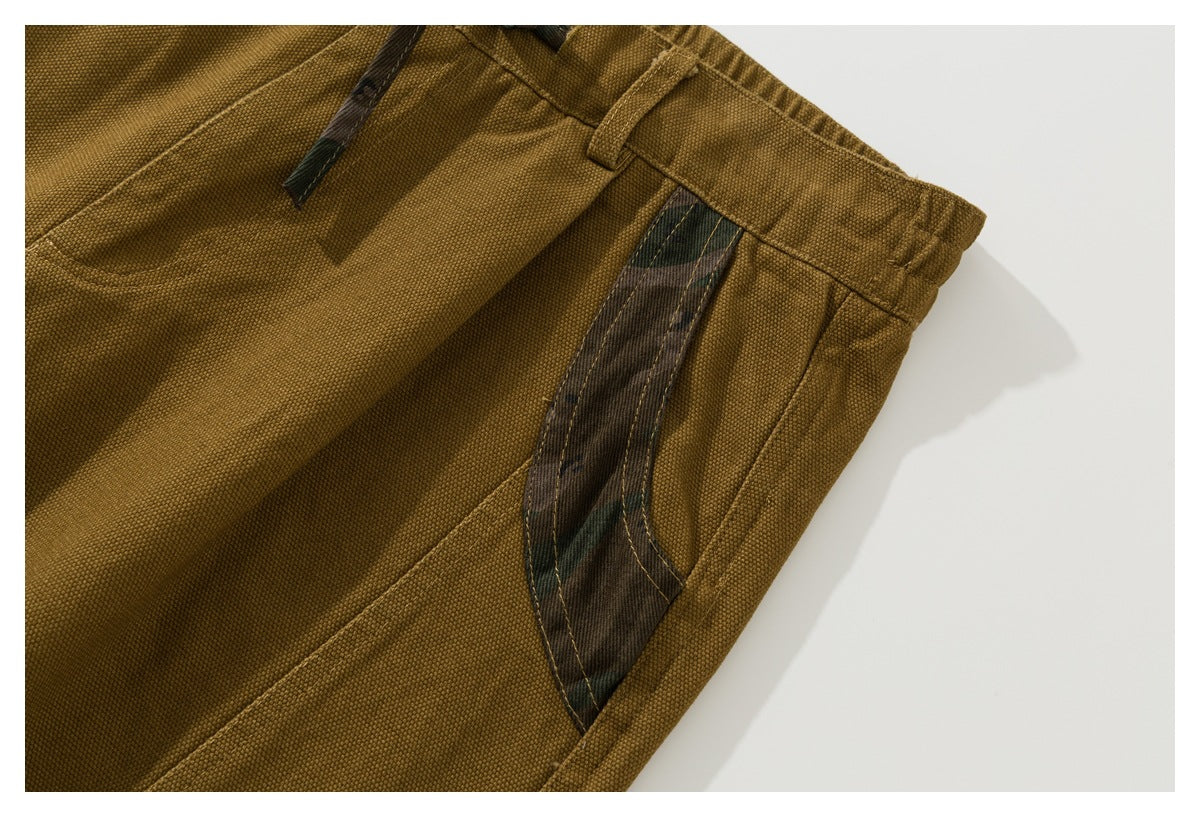 Close-up of a curved side pocket with dark camouflage-print trim on mustard-brown shorts.
