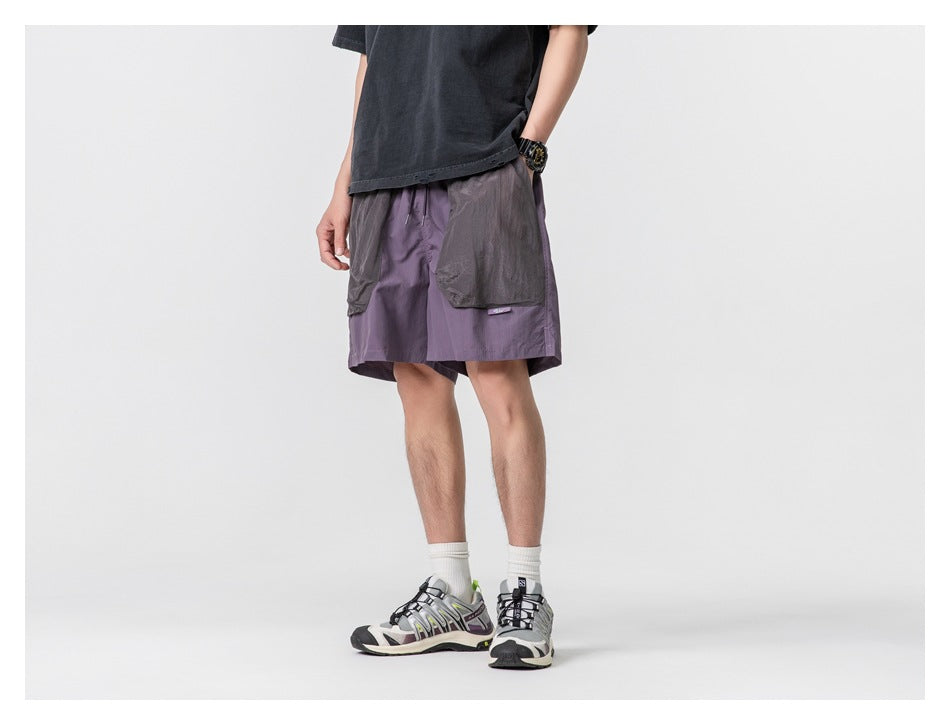 Cropped model wearing muted purple shorts with oversized gray patch pockets, front view.