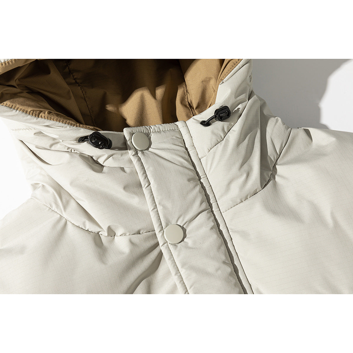 Close-up of a pale gray hooded jacket showing brown lining, black cord toggles, and large snap buttons.