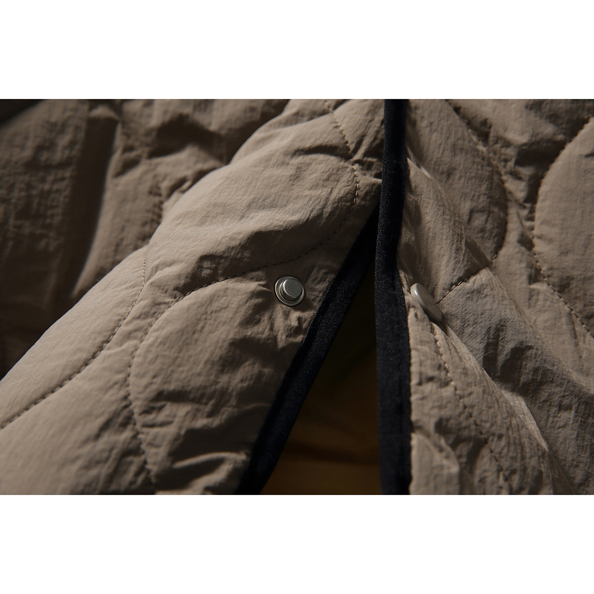 Close-up of the taupe quilted jacket's snap fasteners and black edging.