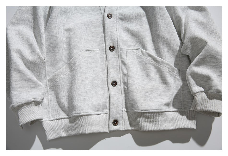 Front view of a light gray cardigan with four dark buttons, two large patch pockets, and ribbed cuffs and hem.