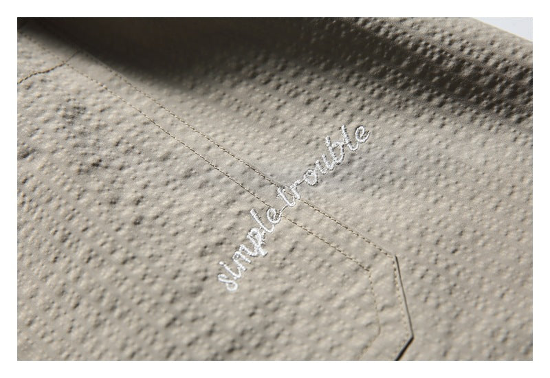 Close-up of beige textured fabric with a stitched seam and white cursive embroidery.
