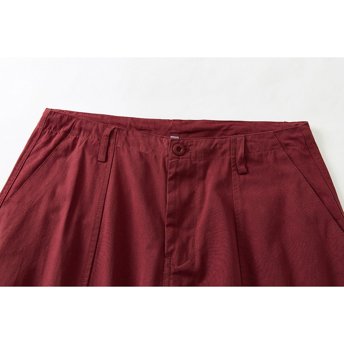 Close-up of burgundy trousers showing the front waistband, button, belt loops, pleats and angled pockets.