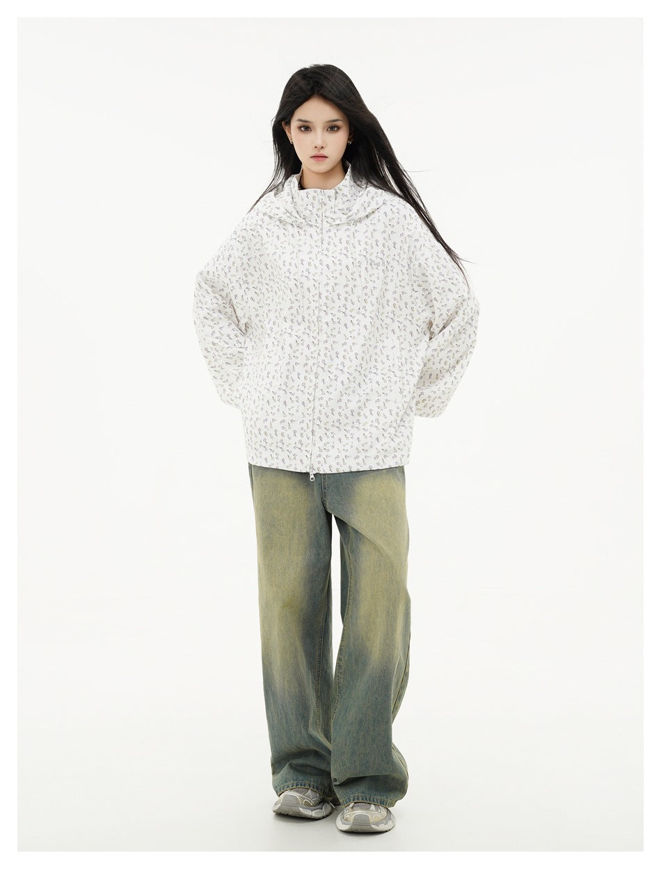 Front view of a model in a white floral-print hooded jacket and loose blue-green jeans.