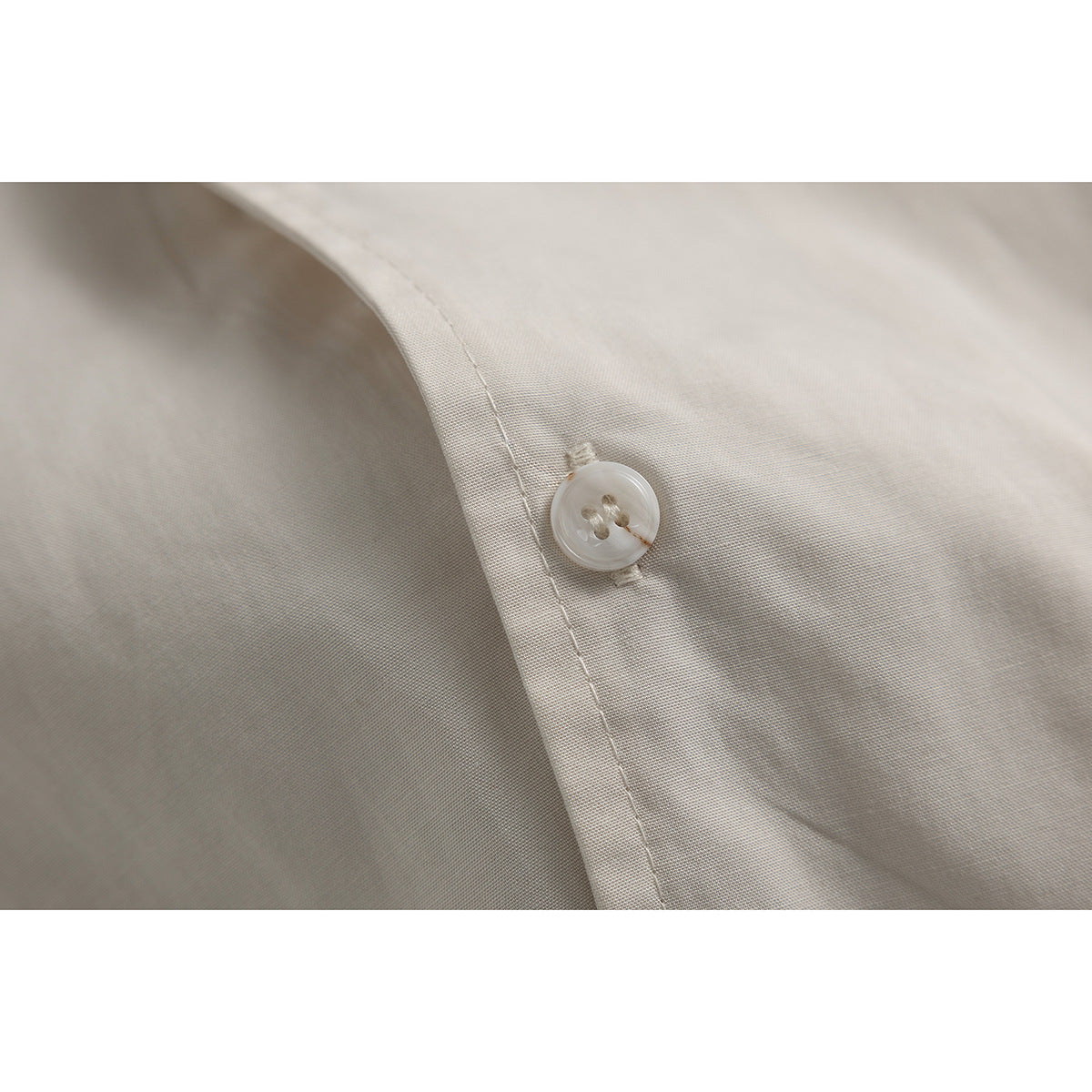 Close-up of a translucent button and stitched placket on ivory shirt fabric.