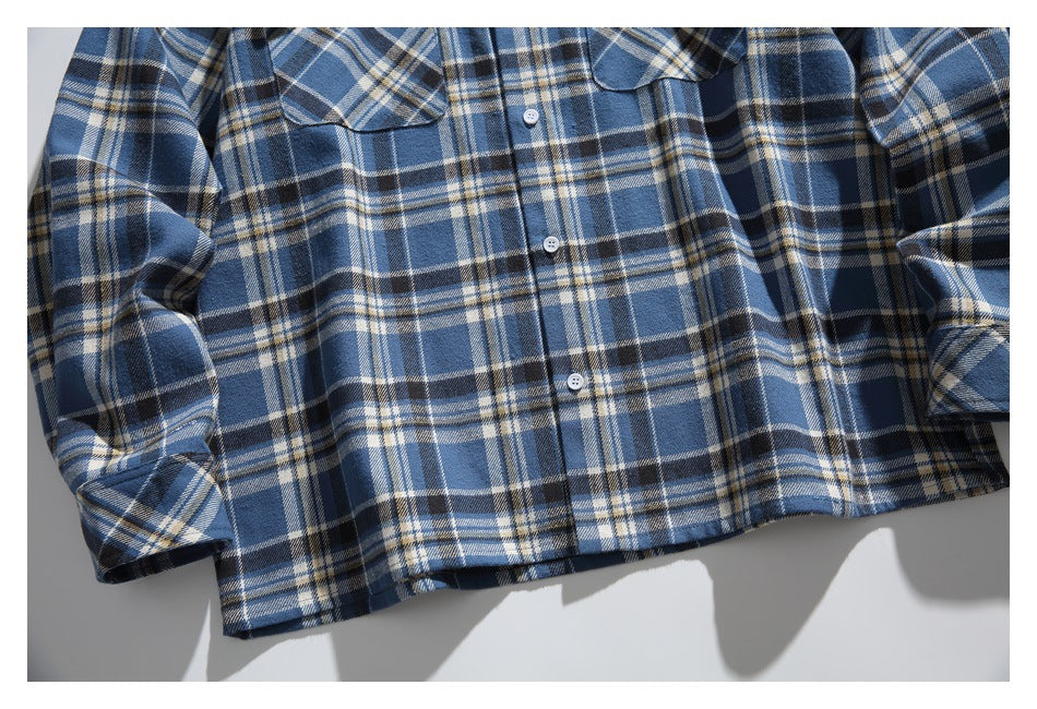 Close-up of the lower front of a blue, navy, and cream plaid button-up shirt.