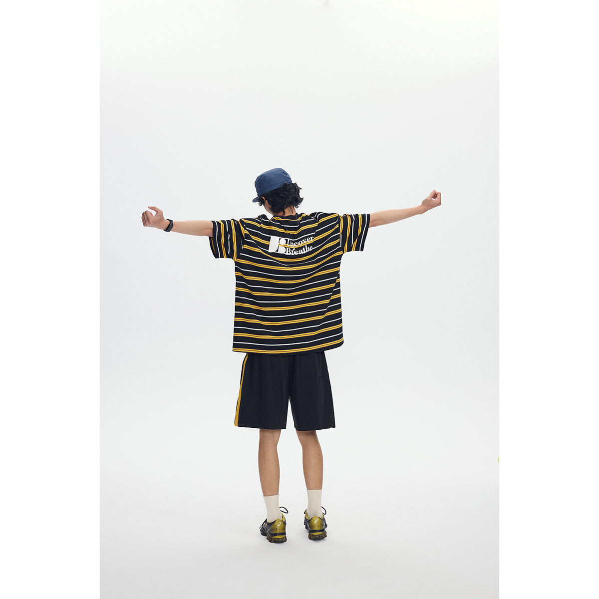 Back view of a model in a black, yellow, and white striped T-shirt with a white back graphic and black shorts.