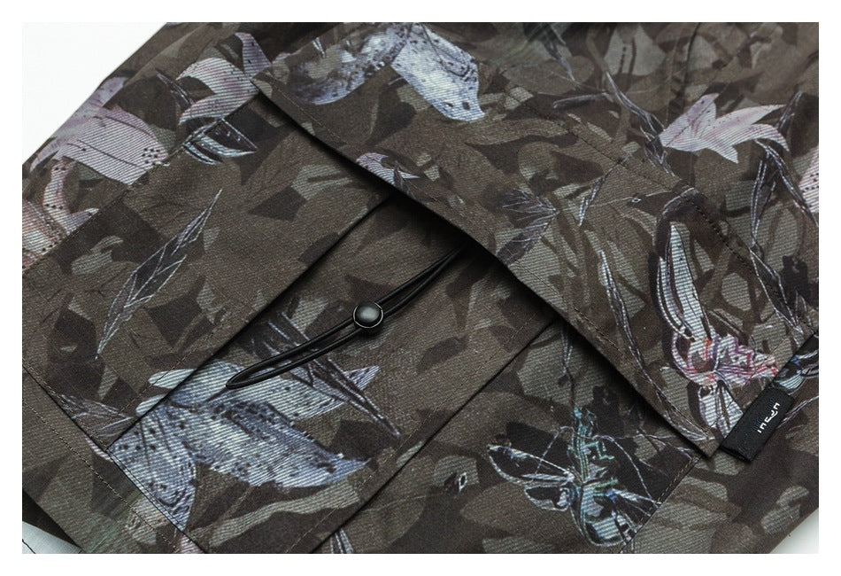 Close-up of a dark printed garment showing a flap pocket with a black elastic loop and button.