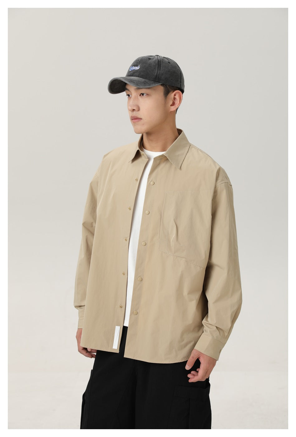 Model wearing an open beige snap-front shirt over a white top, with a single chest pocket.