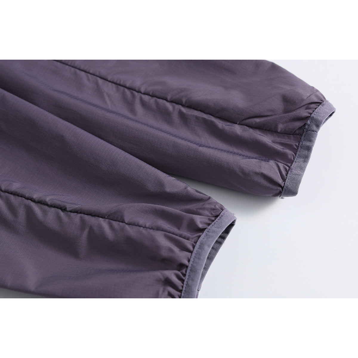 Close-up of two sleeves on a dark purple jacket, showing the gathered cuffs and seam details.
