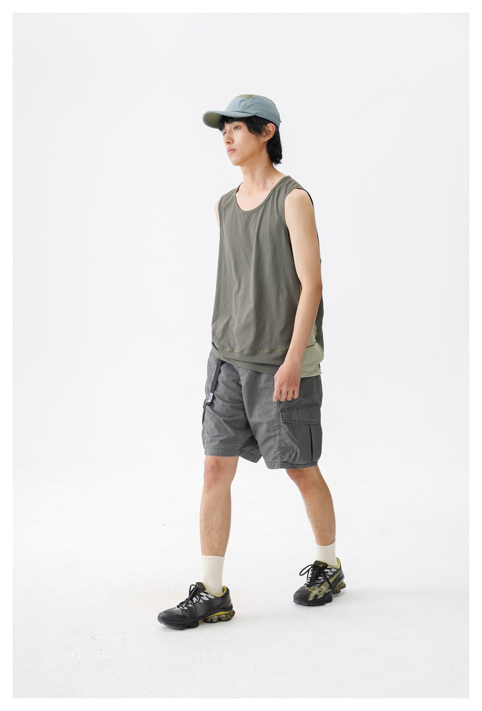 Model wearing a gray-olive sleeveless tank with gray cargo shorts and a blue-gray cap, shown at an angle.