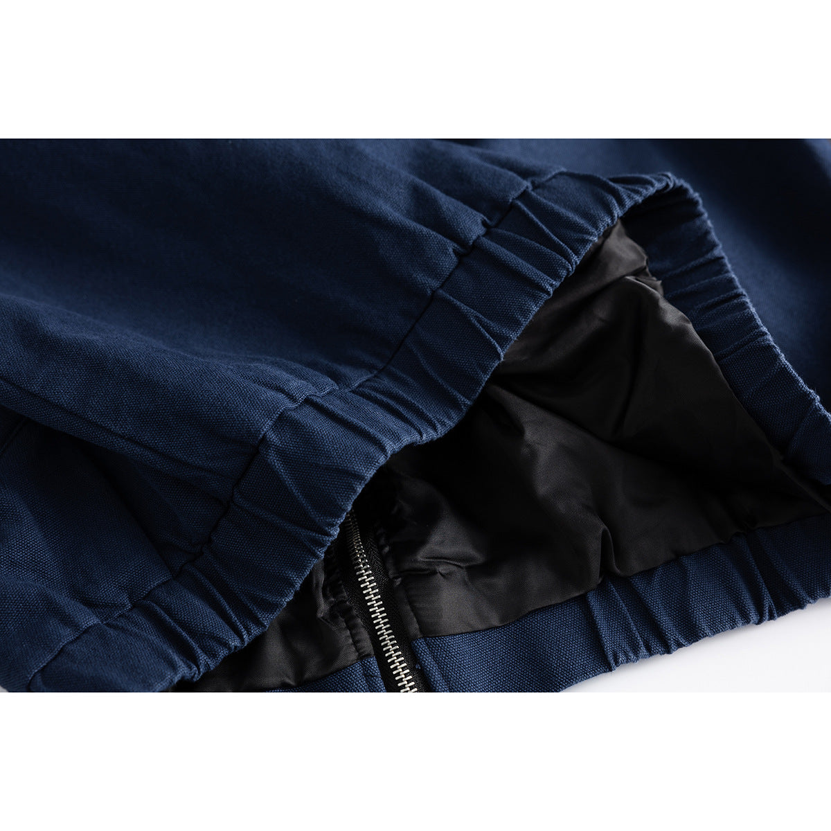 Close-up of a navy jacket's gathered hem and black lining, with part of the zipper visible.