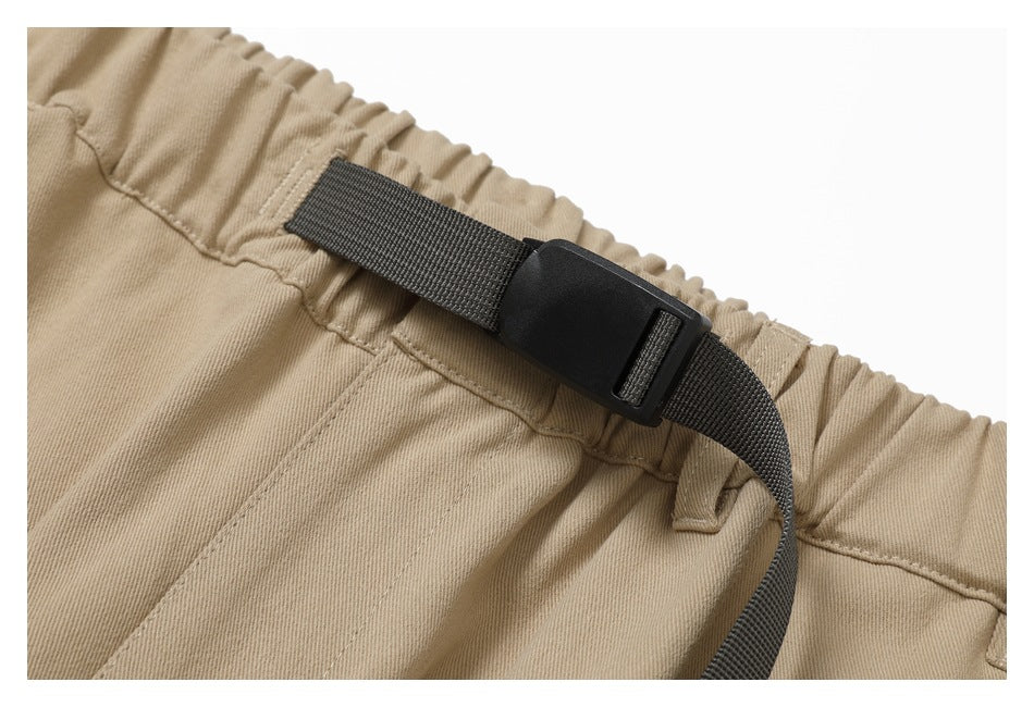 Close-up of the tan pants' gathered waistband and dark webbing belt with a plastic buckle.