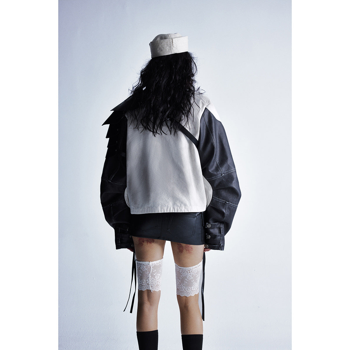 Rear view of a model wearing a cream jacket with black sleeves, a black skirt and lace thigh-highs.