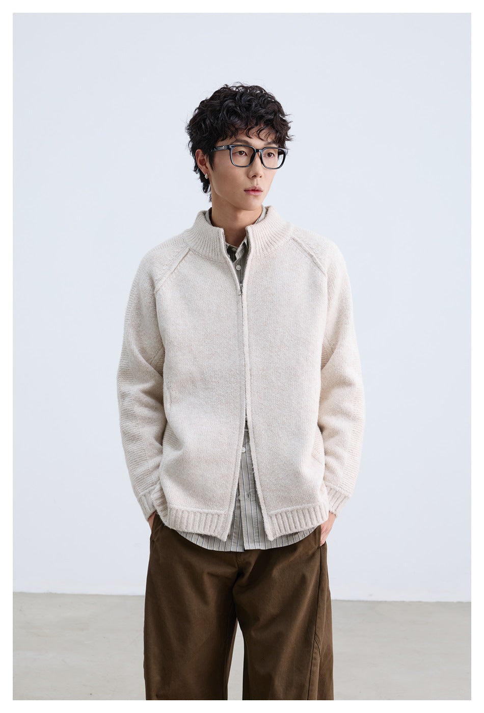 Model wearing apricot zip-up knit cardigan over a striped shirt with brown trousers, front view