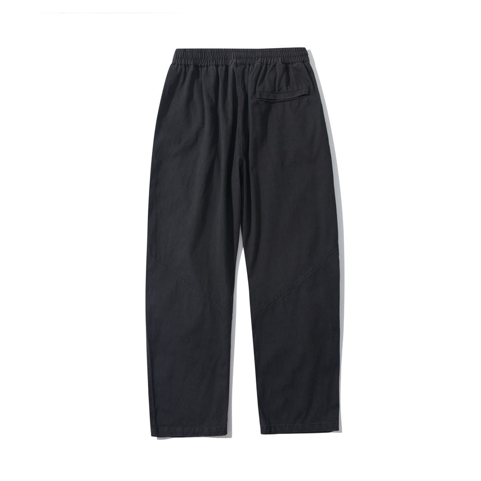 Back view of black loose straight-leg pants with an elastic waistband, a rear pocket, and angled leg seams.