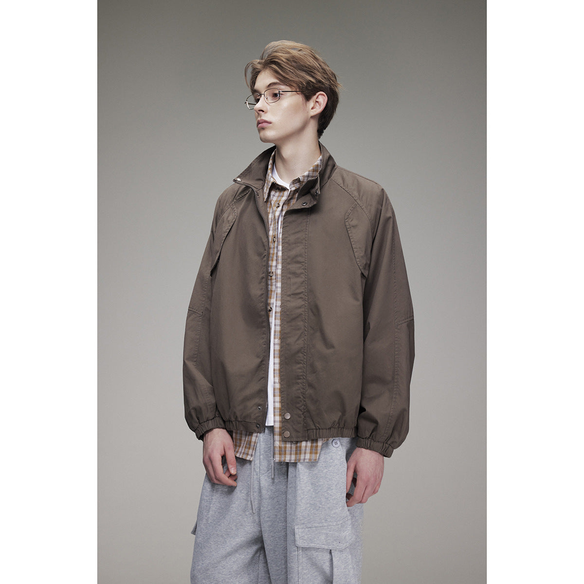 Model wearing a dark taupe zip-front jacket with a raised collar over a plaid shirt.