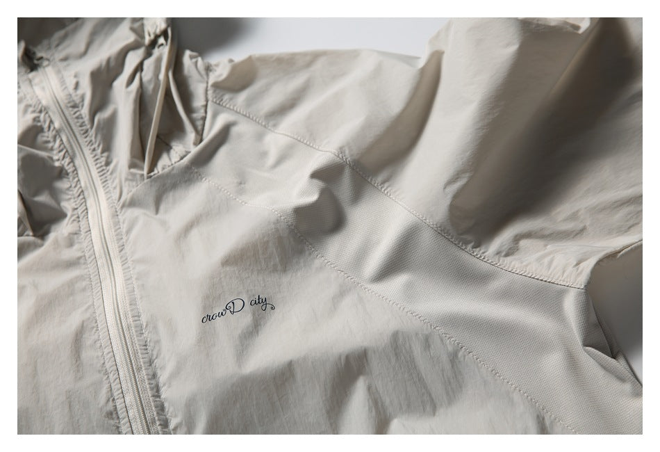 Close-up of a light beige jacket showing a zip front, textured panel stitching and small cursive chest lettering.