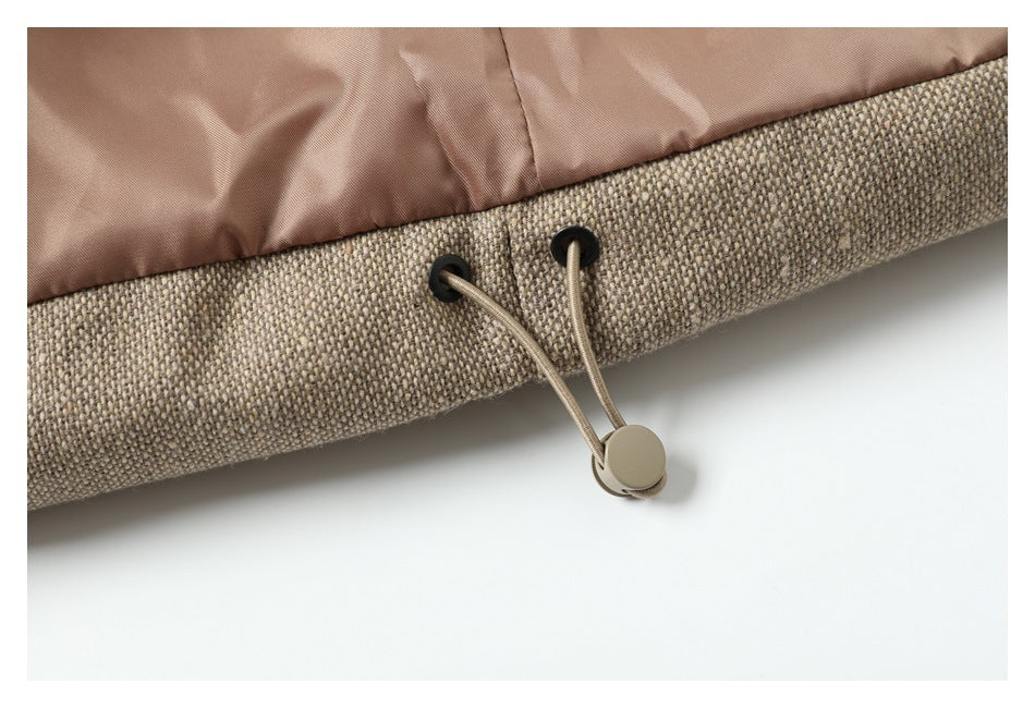 Close-up of a beige woven jacket hem with dusty-rose lining and an adjustable drawcord toggle.