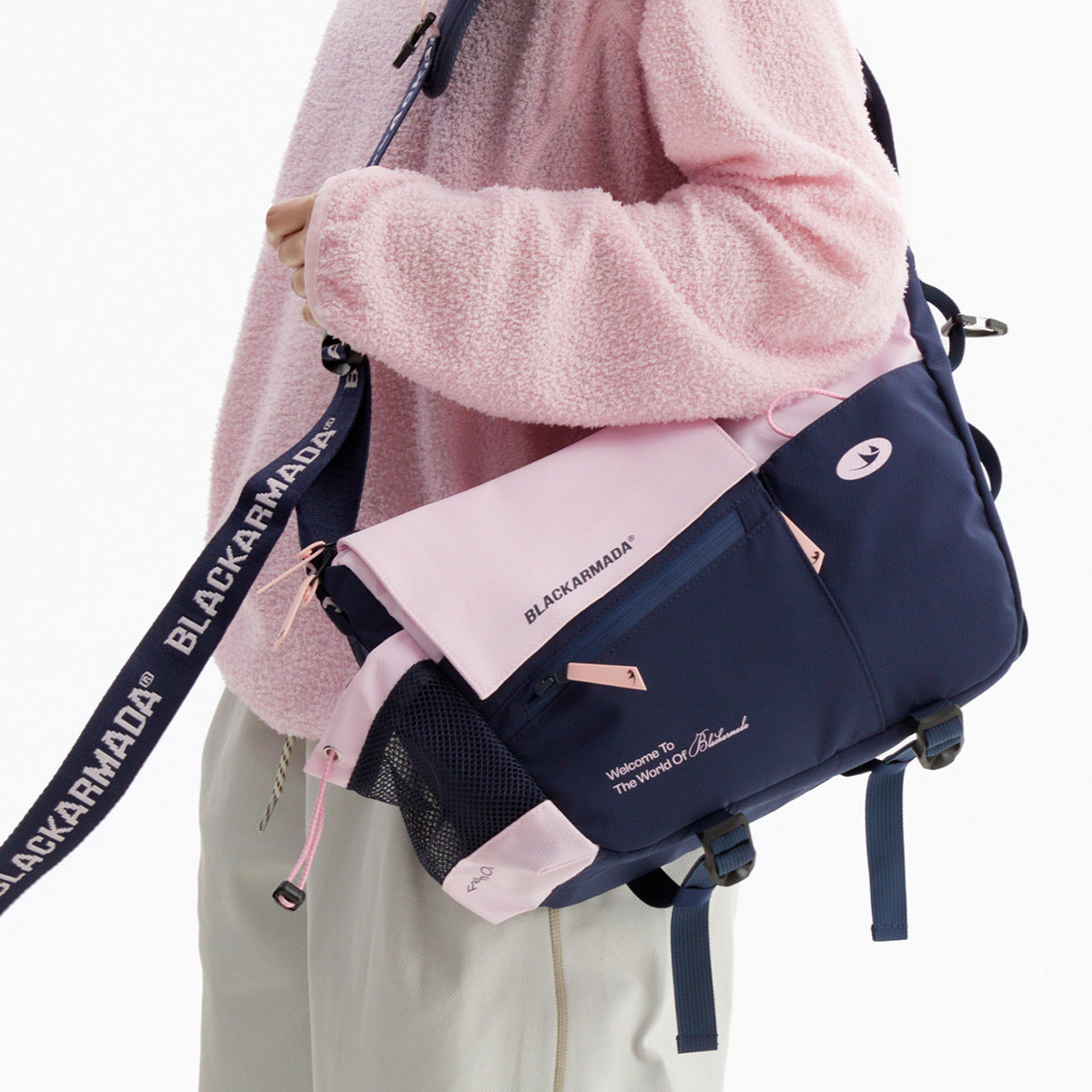 A person wears a navy and pale pink messenger bag with a flap, zip pockets, and mesh side pocket.