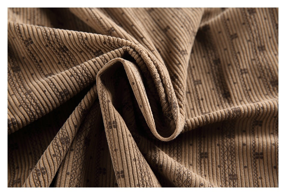 Close-up of brown ribbed fabric gathered into folds, showing its textured weave and scattered dark motifs.