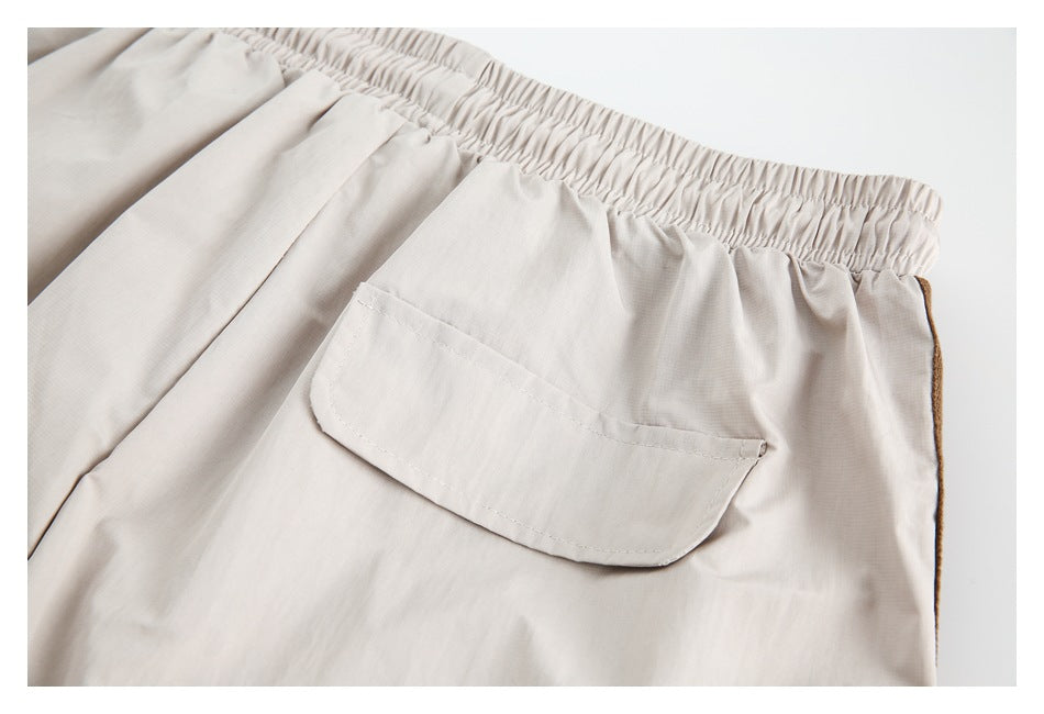 Close-up of the elastic waistband and patch pocket on light beige trousers, with brown trim at the side.