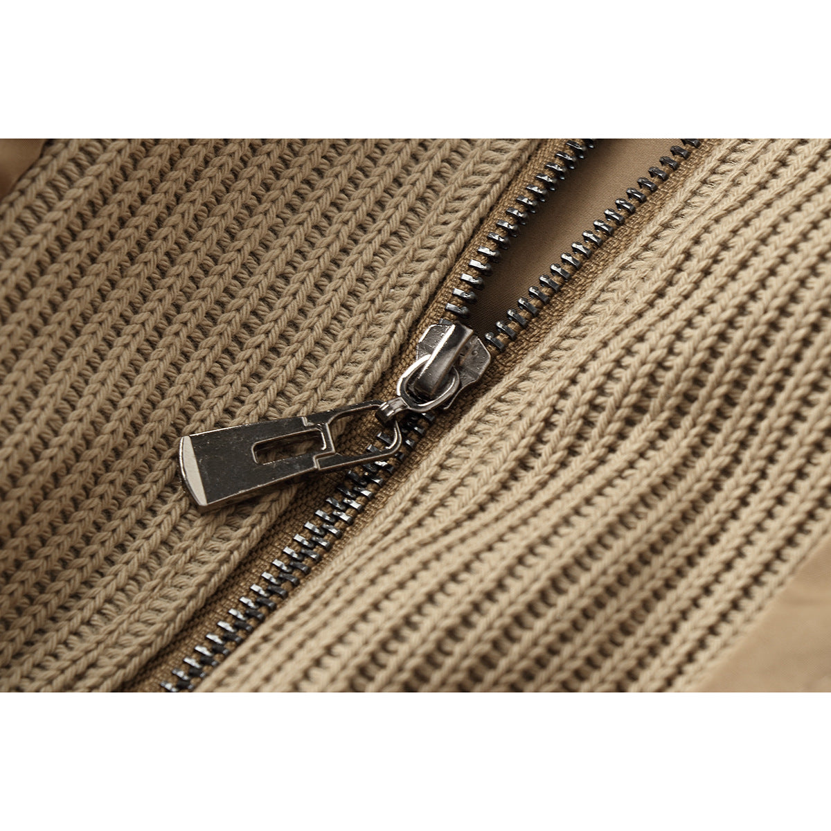 Close-up of the jacket's metal zipper and rib-knit tan fabric.