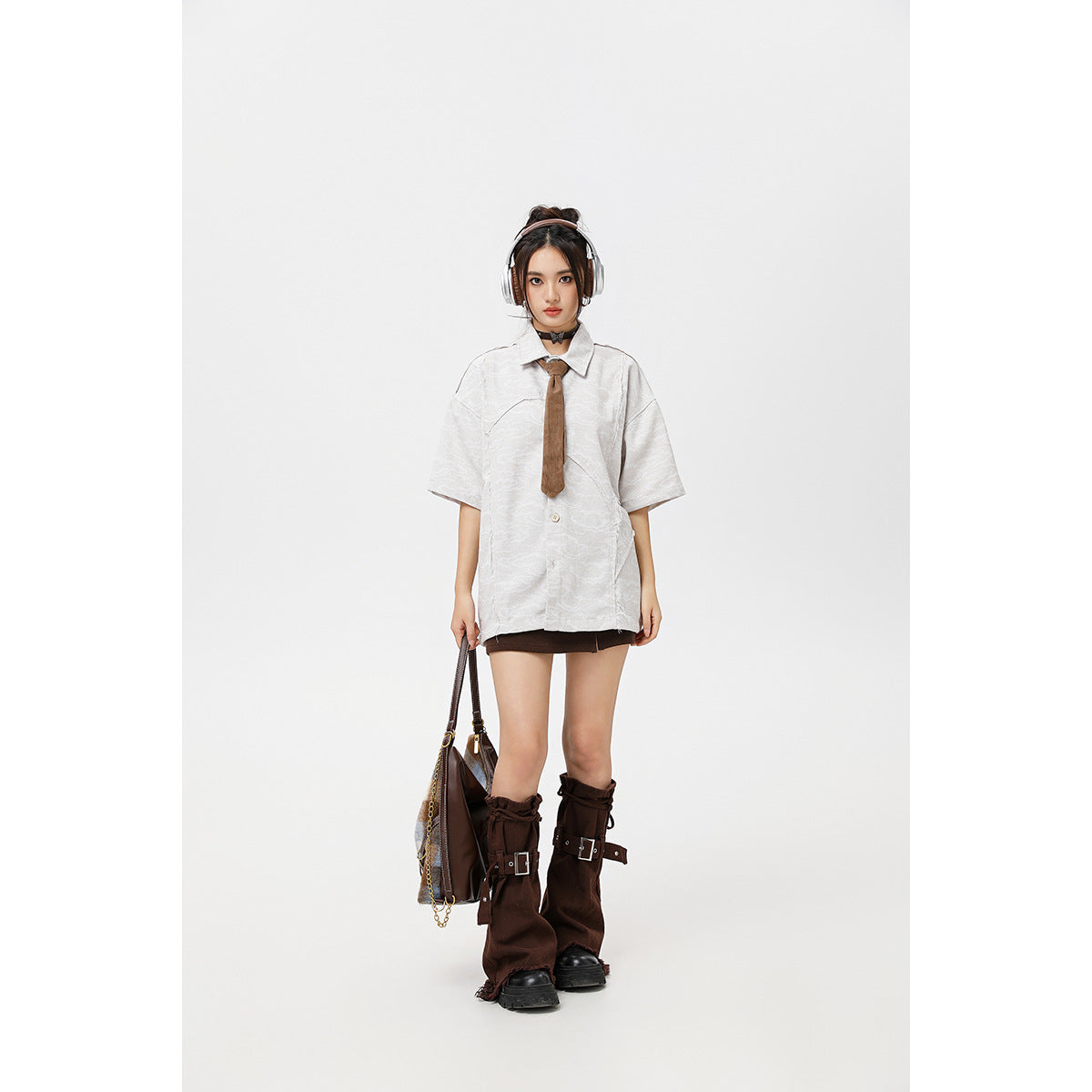 Model wearing an oversized white patterned short-sleeve shirt with a brown tie and dark mini skirt.
