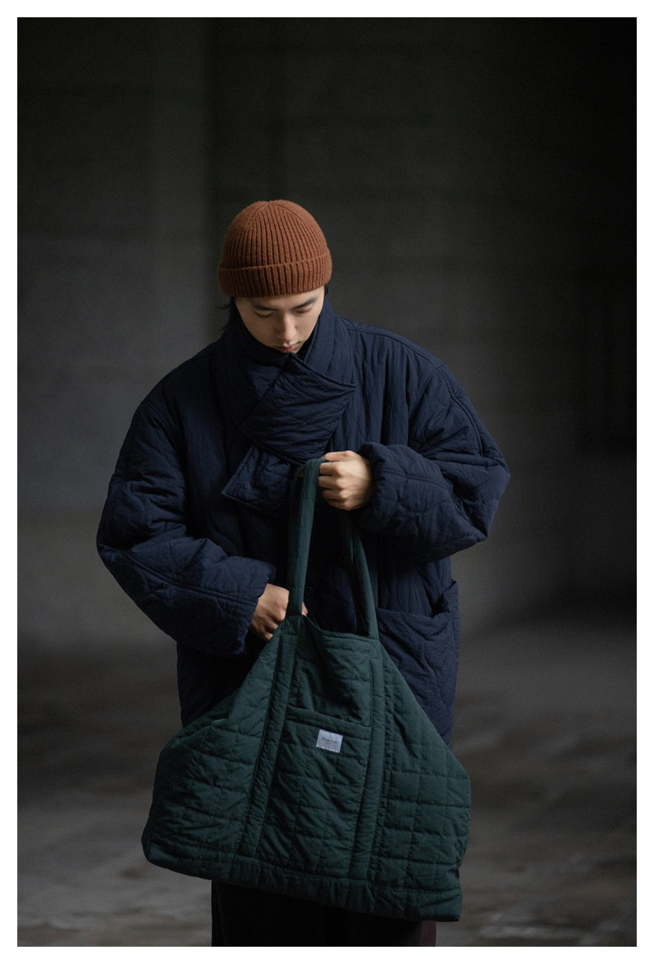 Model wearing a dark navy quilted jacket with a high overlapping collar and roomy sleeves.